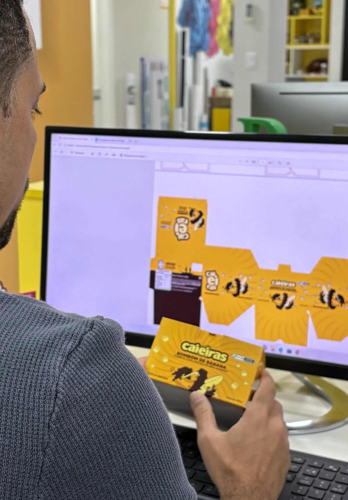 Embalagem do bombom de banana Caieiras ao lado do arquivo dela no monitor da Pixel