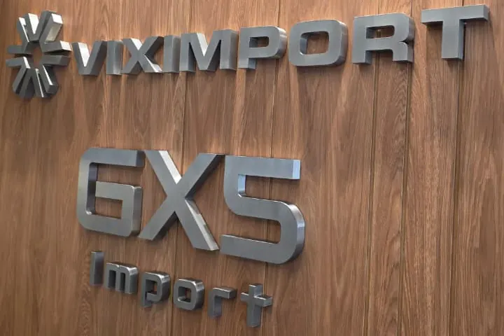 Letreiro da Viximport e da GXS em letras de aço sobre painel de madeira